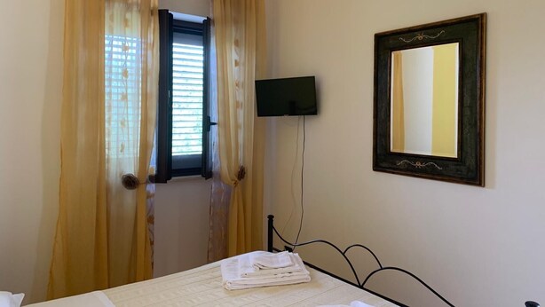 A bedroom with a bed, a television, a mirror, and a window with curtains. - Agriturismo Perla del Salento, just a few steps from the sea and the beautiful beaches (Puglia)