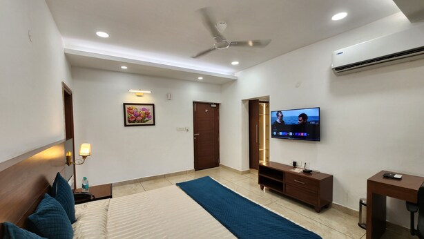 A hotel room with a bed, a TV, a ceiling fan, and a wall-mounted air conditioner. - Red Bishop Tourist Complex (Panchkula)