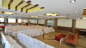 A conference room with rows of white chairs, a stage with a red table, and a modern ceiling design. - Red Bishop Tourist Complex (Panchkula)