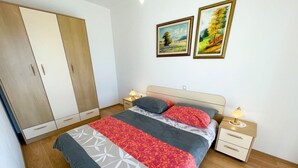 Un dormitorio con cama, mesitas de noche, un armario y dos cuadros en la pared.