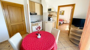 Una habitación compacta con una mesa de comedor, sillas, kitchenette, cama y televisor.