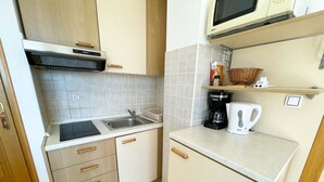 Cocina compacta con lavamanos, estufa y microondas. Hay armarios con tiradores de madera y una encimera con hervidor y cafetera.