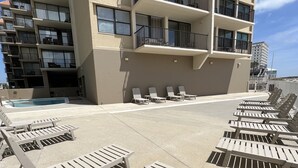 Tagterrasse med pool, liggestole og en bygning med flere altaner.