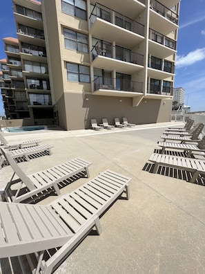 Un espace aménagé au bord de la piscine, avec des chaises longues et un bâtiment doté de nombreux balcons.