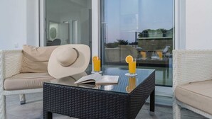 A modern outdoor seating area with a wicker table, a sofa, and a large window. - Vigla Kiotari - B, Villa (Greece)