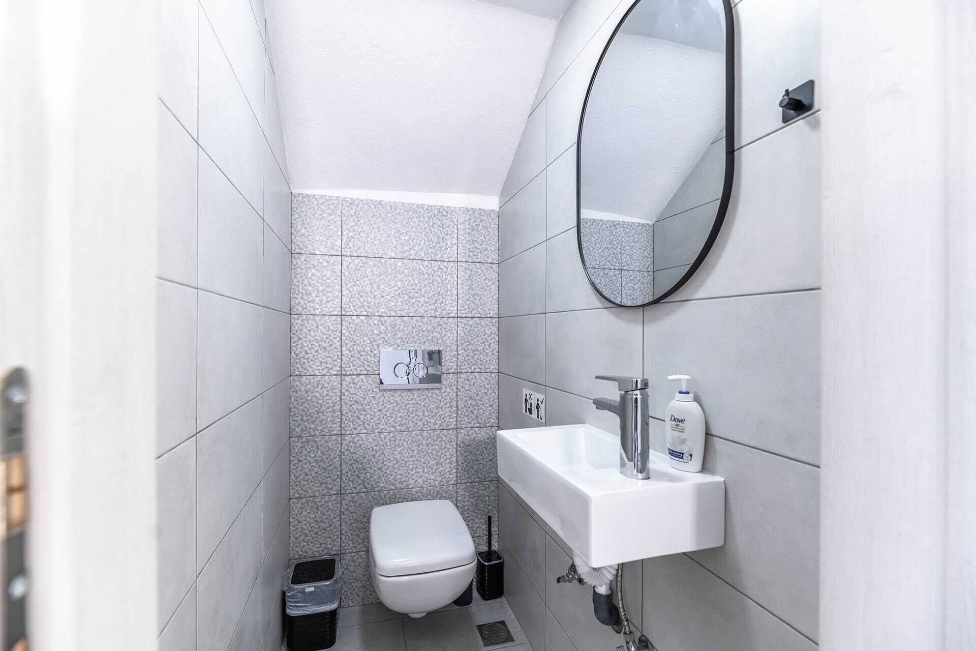 Een kleine, moderne badkamer met toilet, wastafel en spiegel.