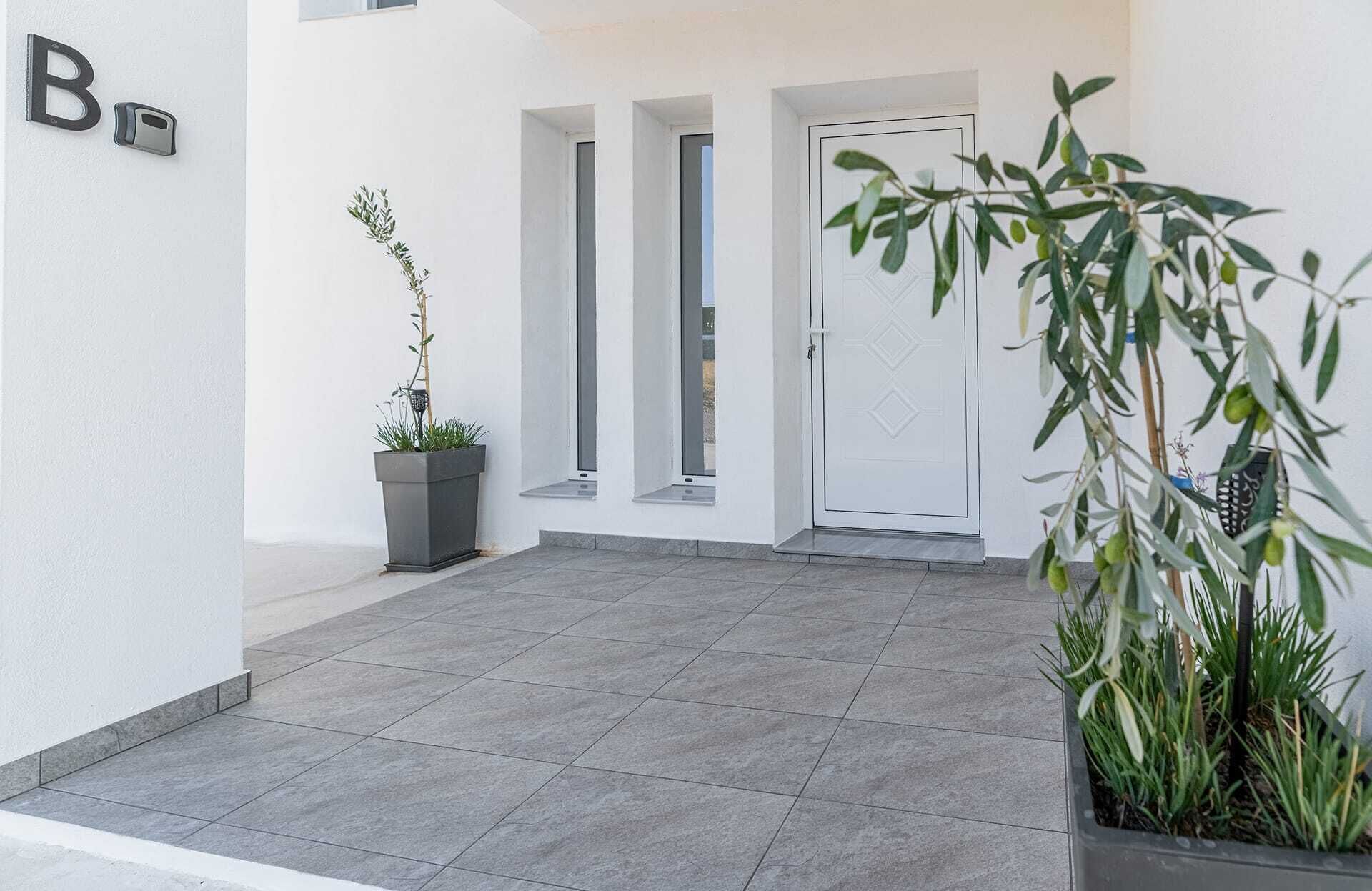 A clean, modern entrance with a white door, a potted plant, and a 'B' sign on the wall.