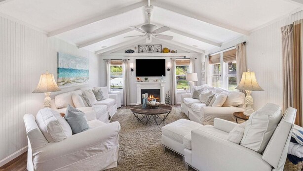 Un salon spacieux, meublé de blanc, avec une cheminée et un ventilateur de plafond.