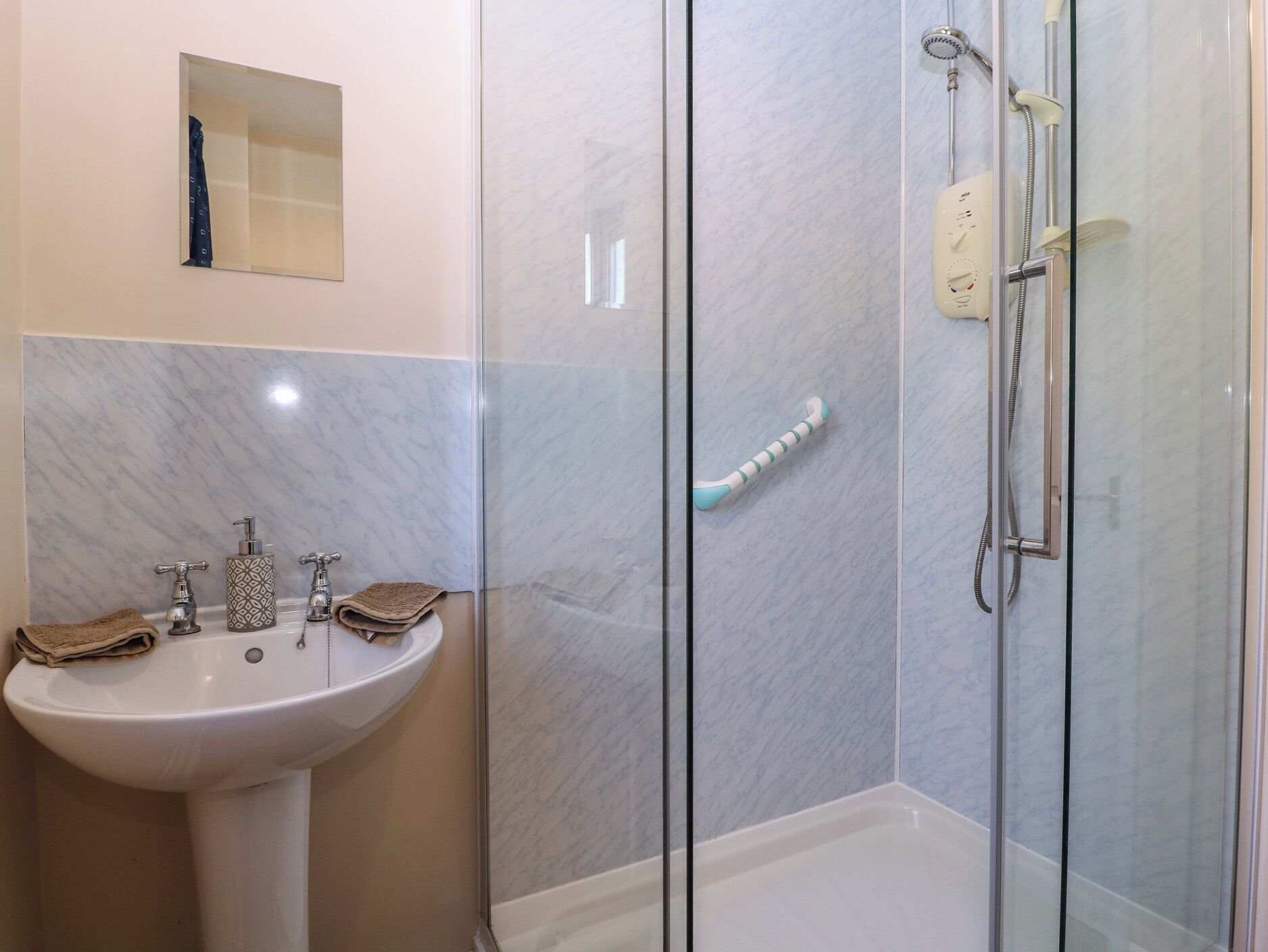 A bathroom with a glass-enclosed shower, a sink, and a mirror.