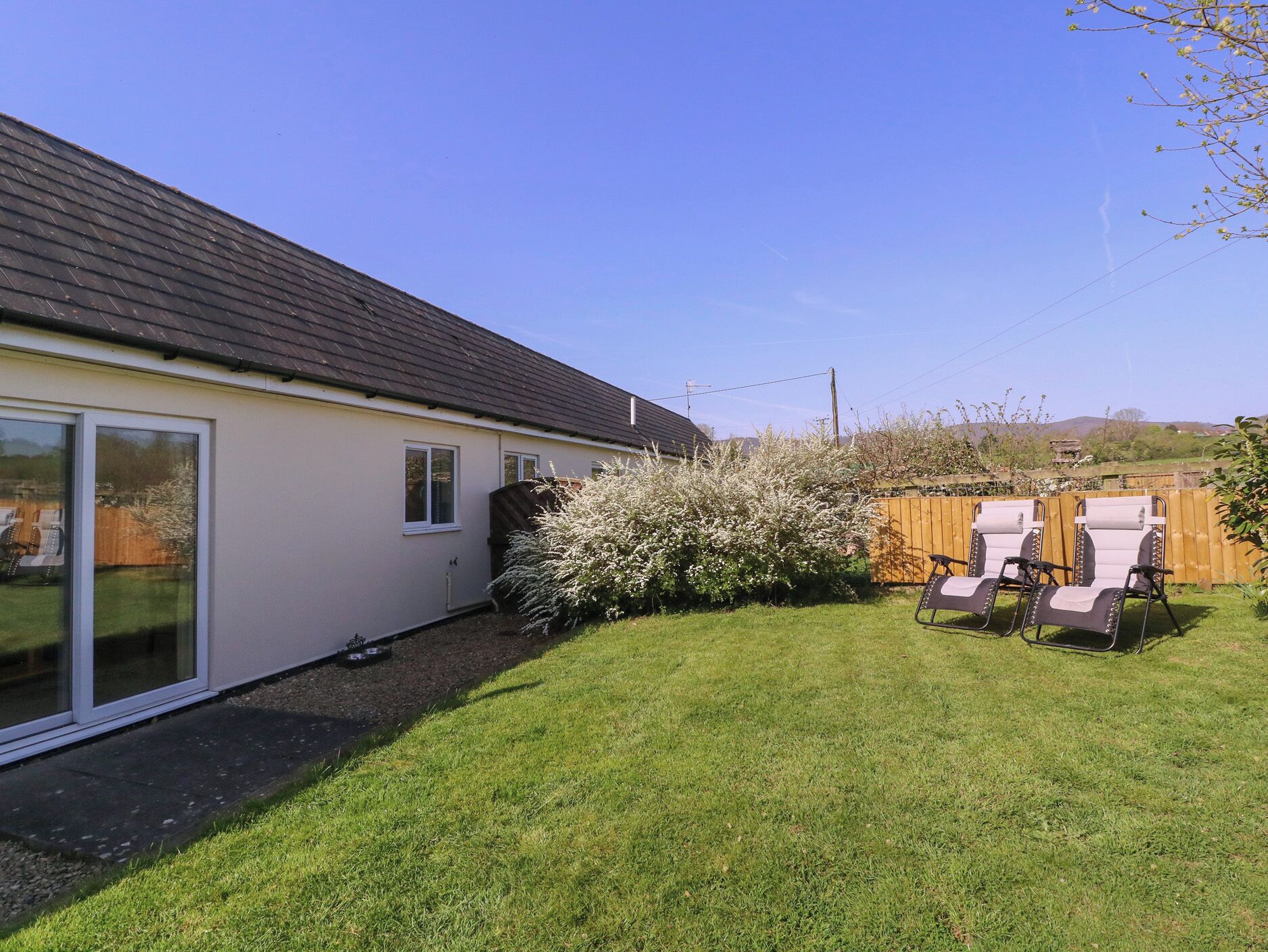 A house with a sloped roof, a large sliding glass door, a fenced yard, and outdoor seating.