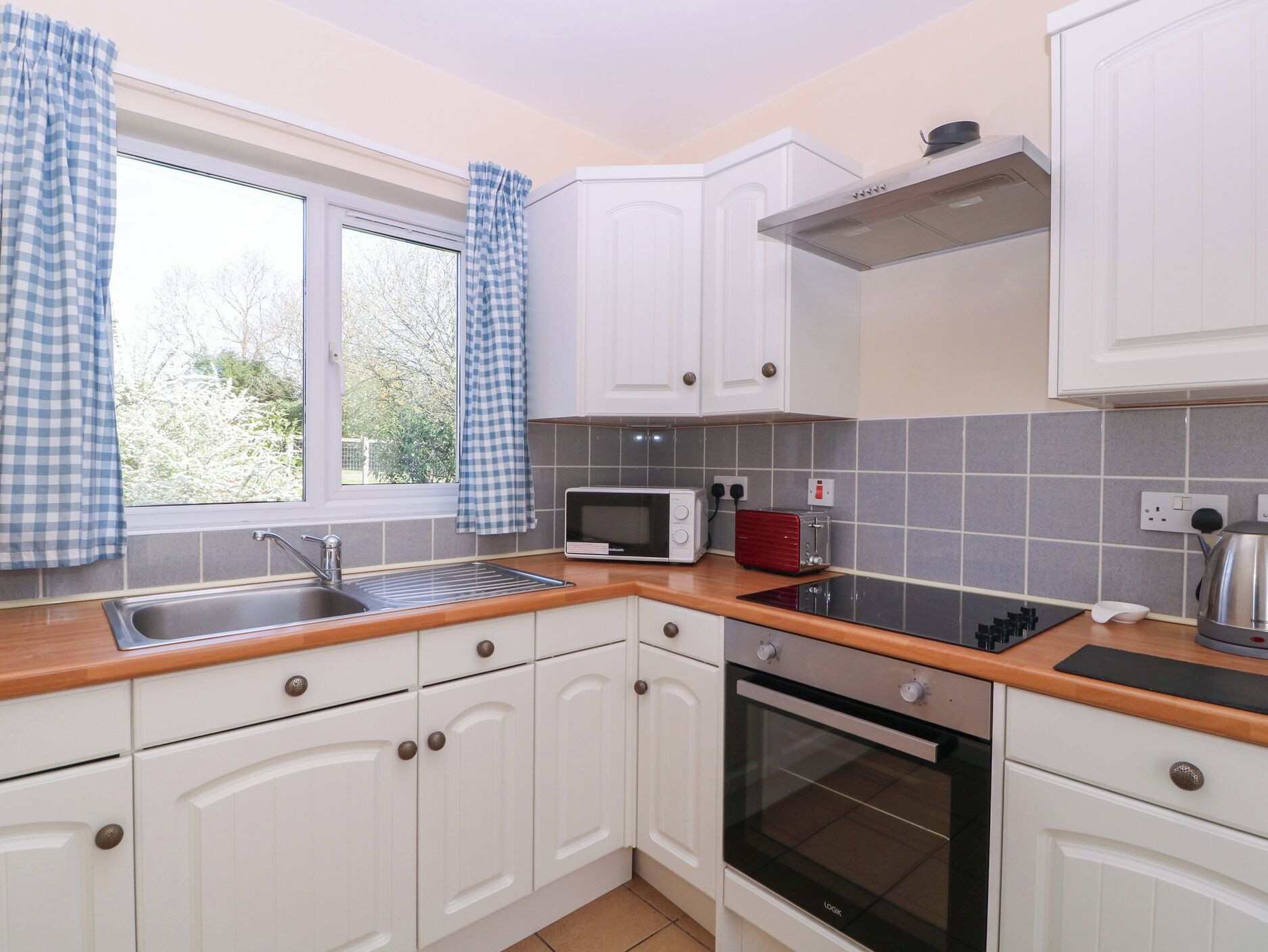 A kitchen with white cabinets, a microwave, a toaster, an oven, and a window with curtains.