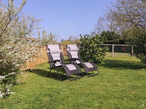 Two outdoor lounge chairs in a grassy backyard with a wooden fence and flowering trees. - The Turbles - Wagtail (Malvern)