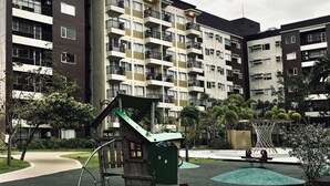 A playground with a climbing structure and a small slide, surrounded by a landscaped area with trees and a water feature. - 7 The Metro View Dream Loft (Iloilo)