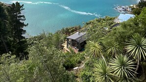 Eine Küstenlandschaft mit freiem Blick auf das Meer, ein kleines Gebäude mit Balkon und umgebender Bepflanzung.