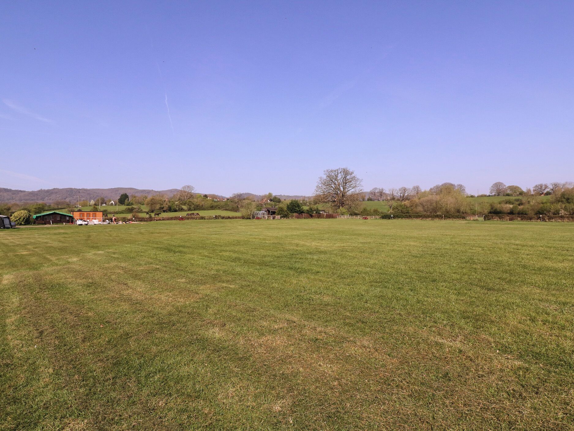 A wide grassy field with a few buildings in the distance.