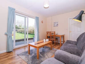 A living room with a sofa, a wooden table, and a dining table with chairs. - The Turbles - Swallows Nest (Malvern)