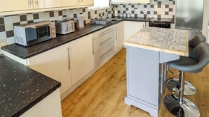 Une cuisine moderne avec des meubles blancs, un plan de travail noir, un four à micro-ondes, un grille-pain et un tabouret de bar.