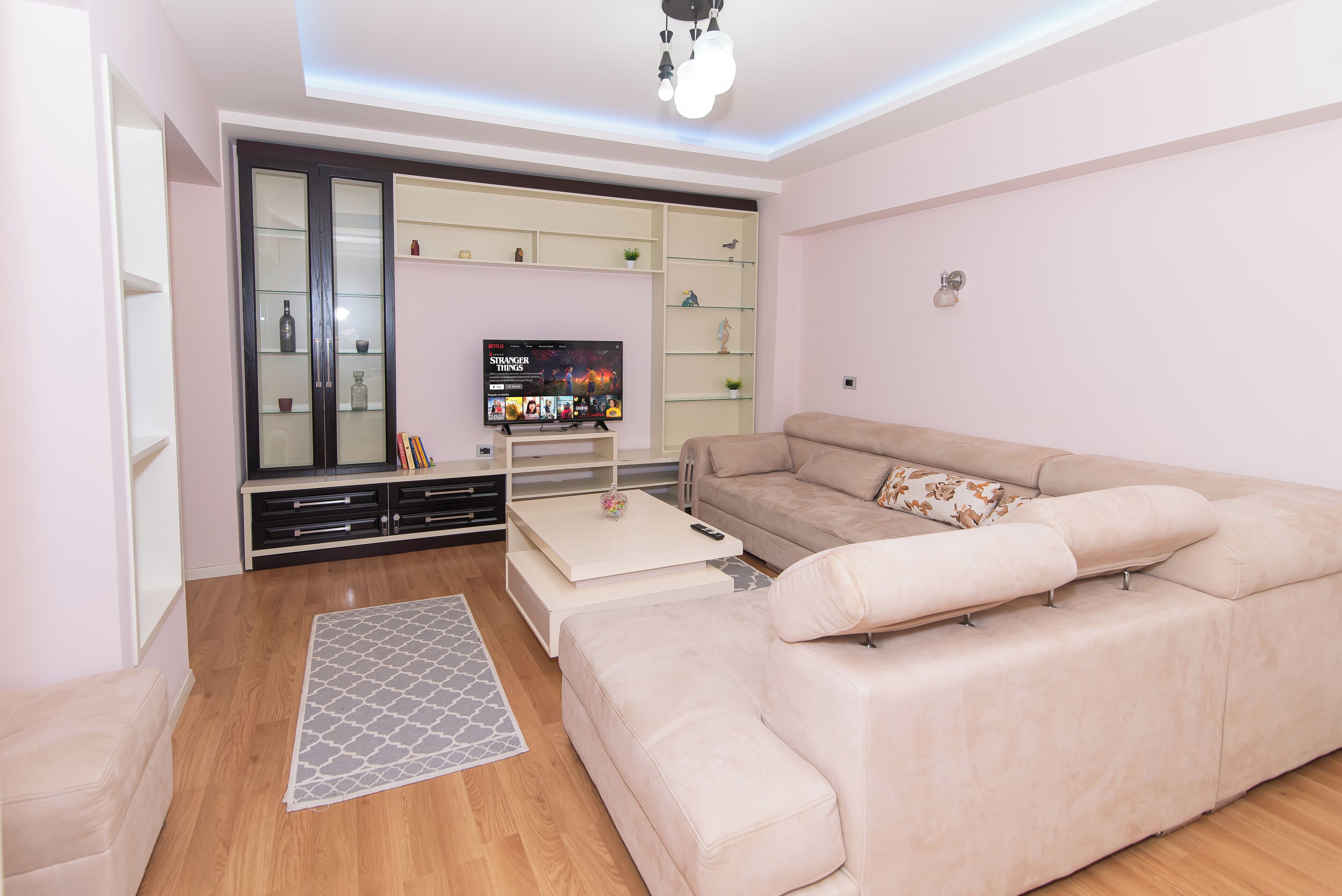 Un salon moderne avec un canapé beige, un téléviseur à écran plat et une étagère avec une façade en verre.