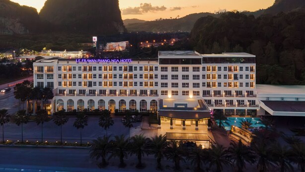 A multi-story hotel with a swimming pool, surrounded by palm trees and mountains. - Le Erawan Hotel (Phang Nga)