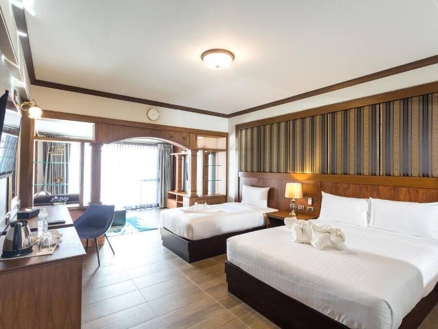 Una habitación de hotel con dos camas, un escritorio con una silla, un televisor y un ventanal grande.