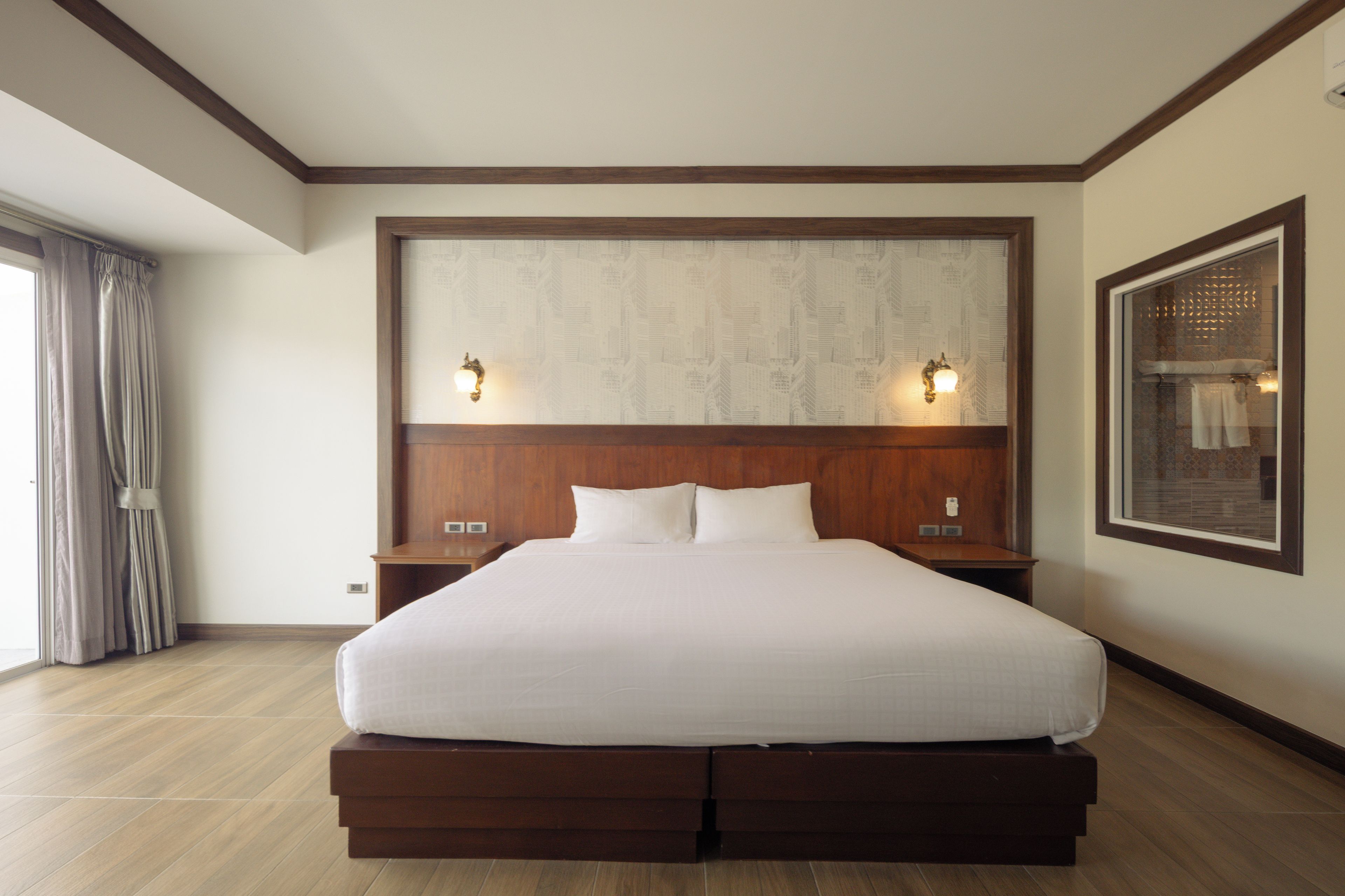 Una cama grande con cabecera de madera, dos mesitas de noche y un ventanal con cortinas.