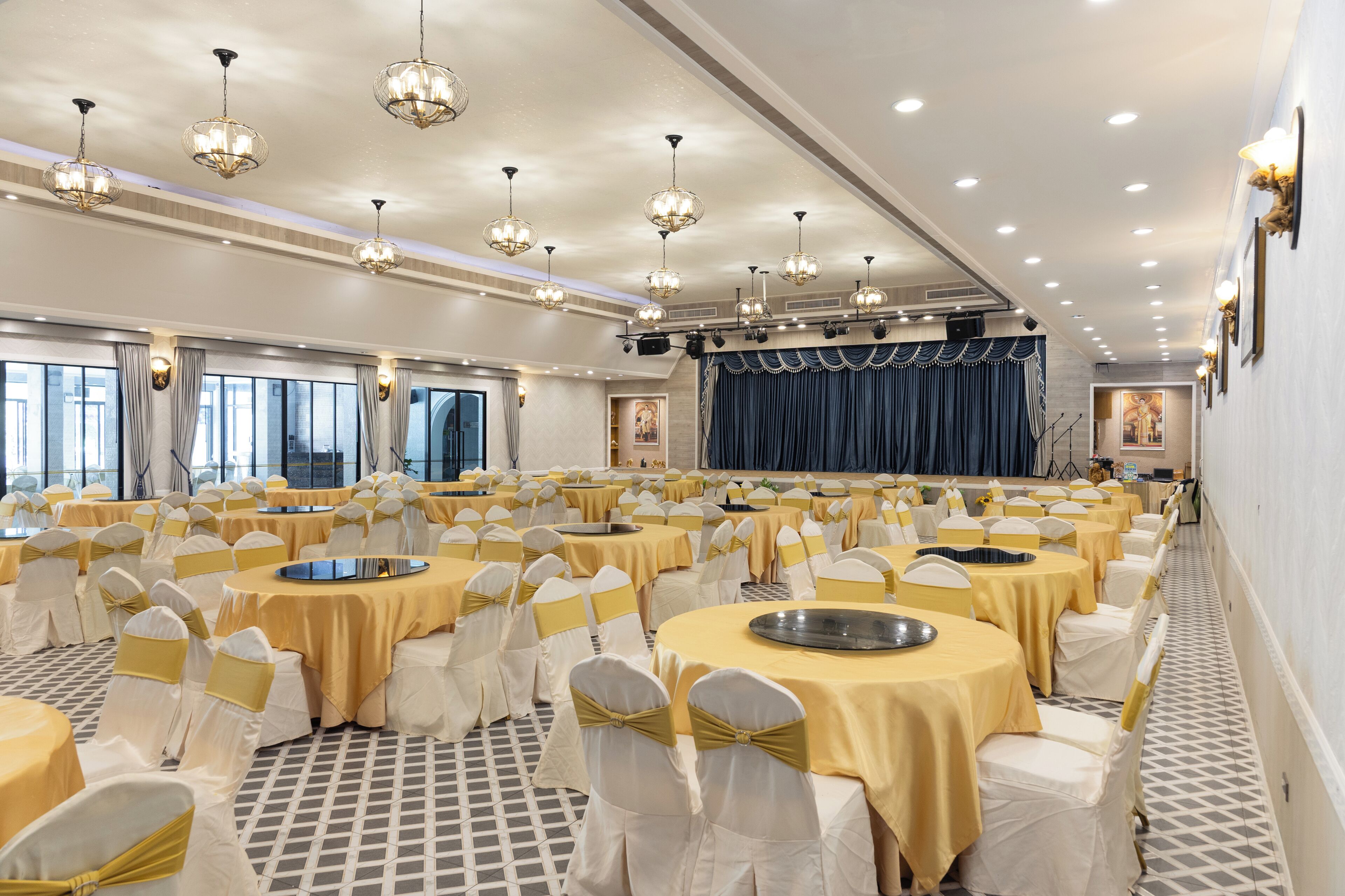 A banquet hall with round tables, white chairs with gold sashes, and chandeliers.