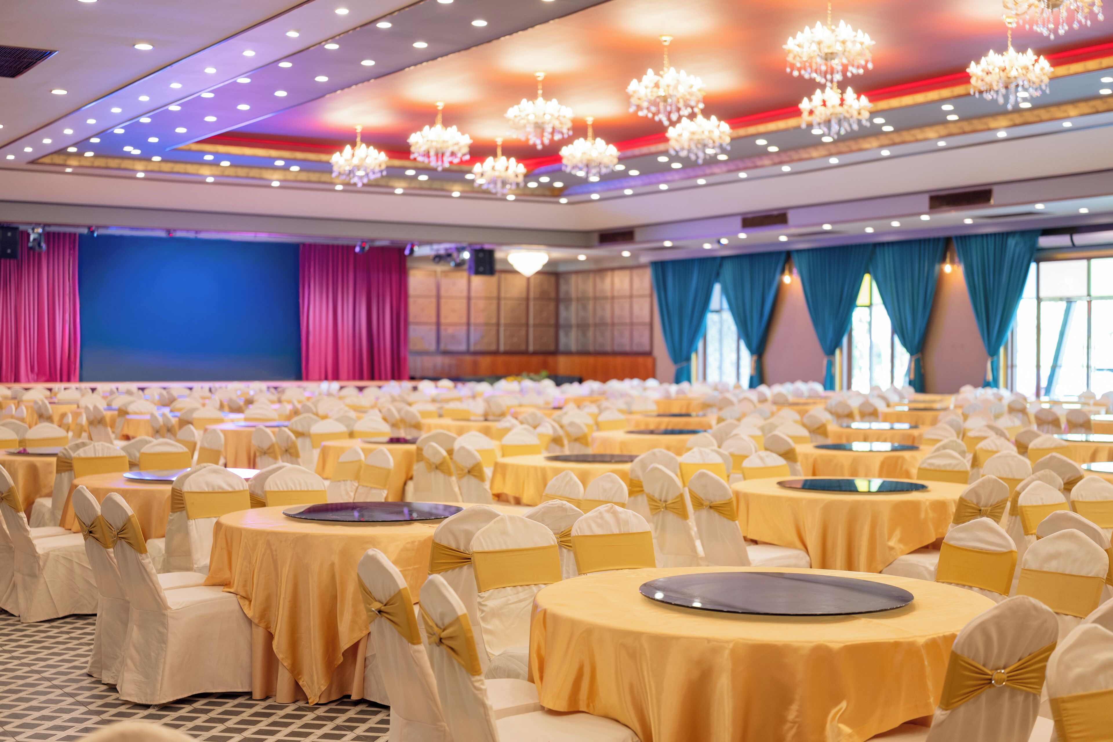A banquet hall with round tables, chairs with yellow sashes, and chandeliers.