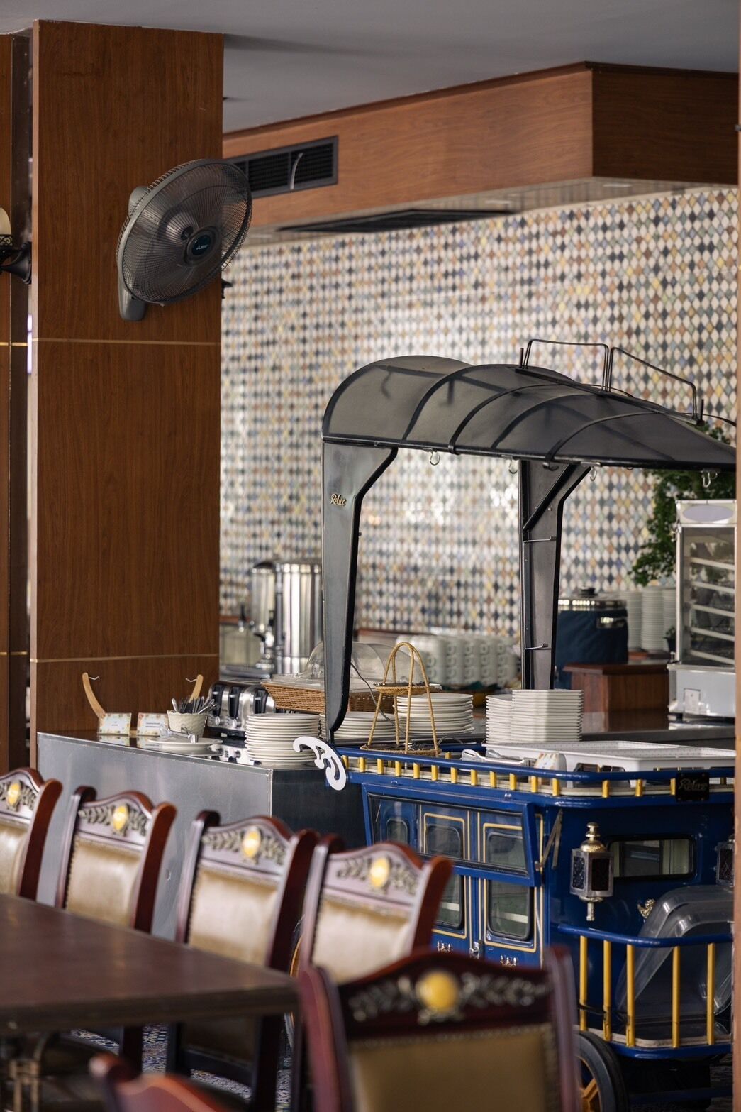 A restaurant with a blue and gold train-themed bar area, a patterned tile backsplash, and a fan mounted on the wall.