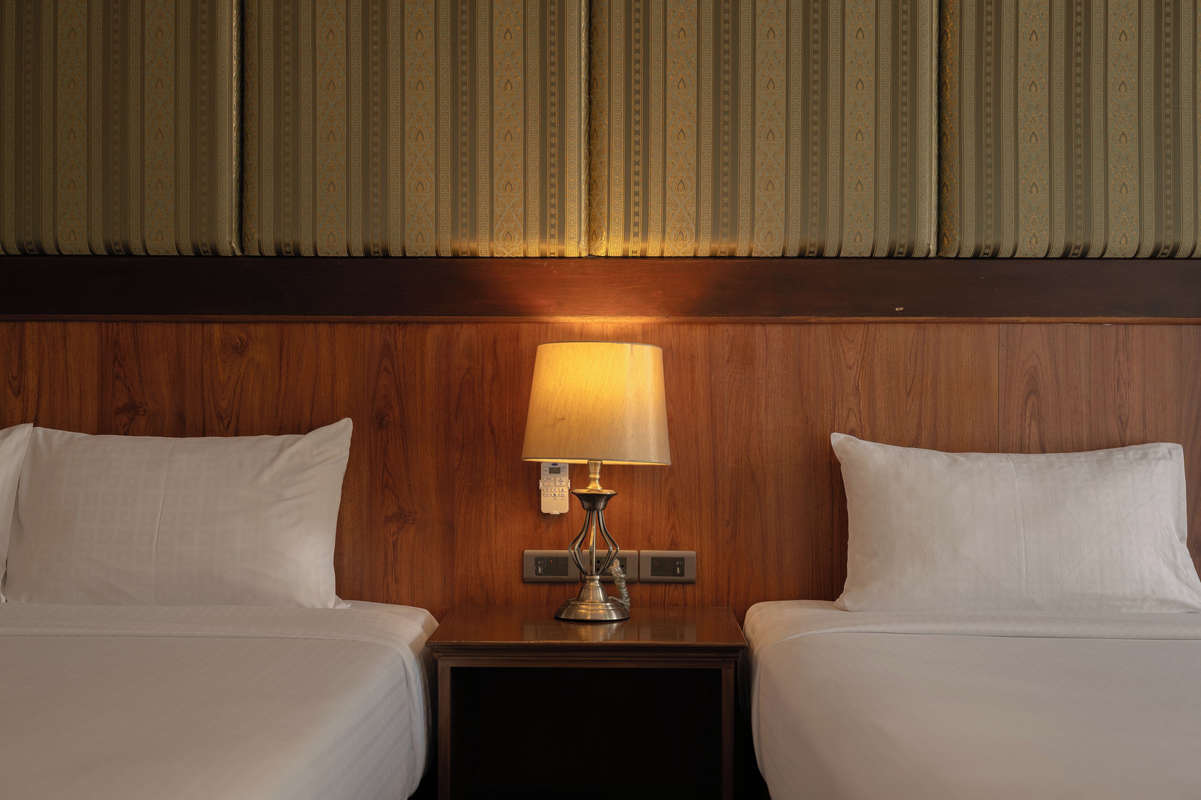 A hotel room with two beds, a nightstand with a lamp, and a wooden headboard.