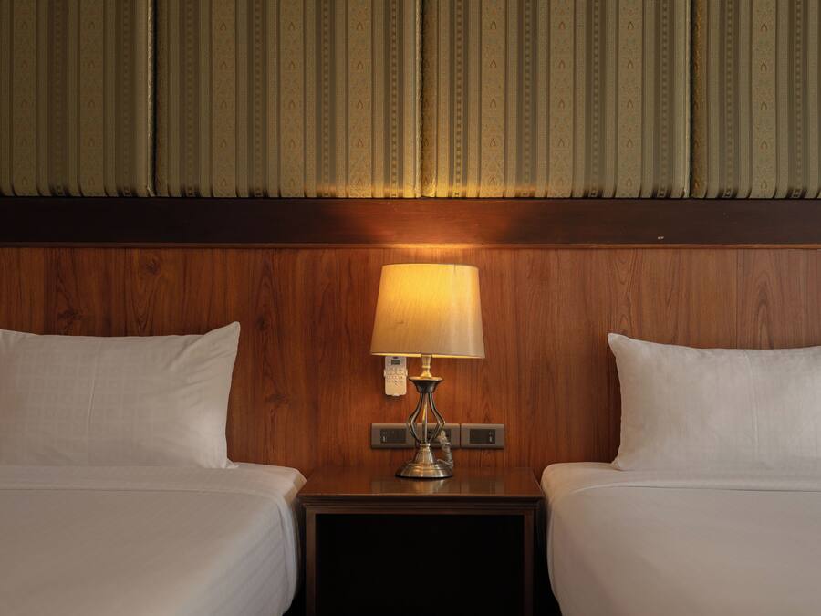 A hotel room with two beds, a nightstand with a lamp, and a wooden headboard.
