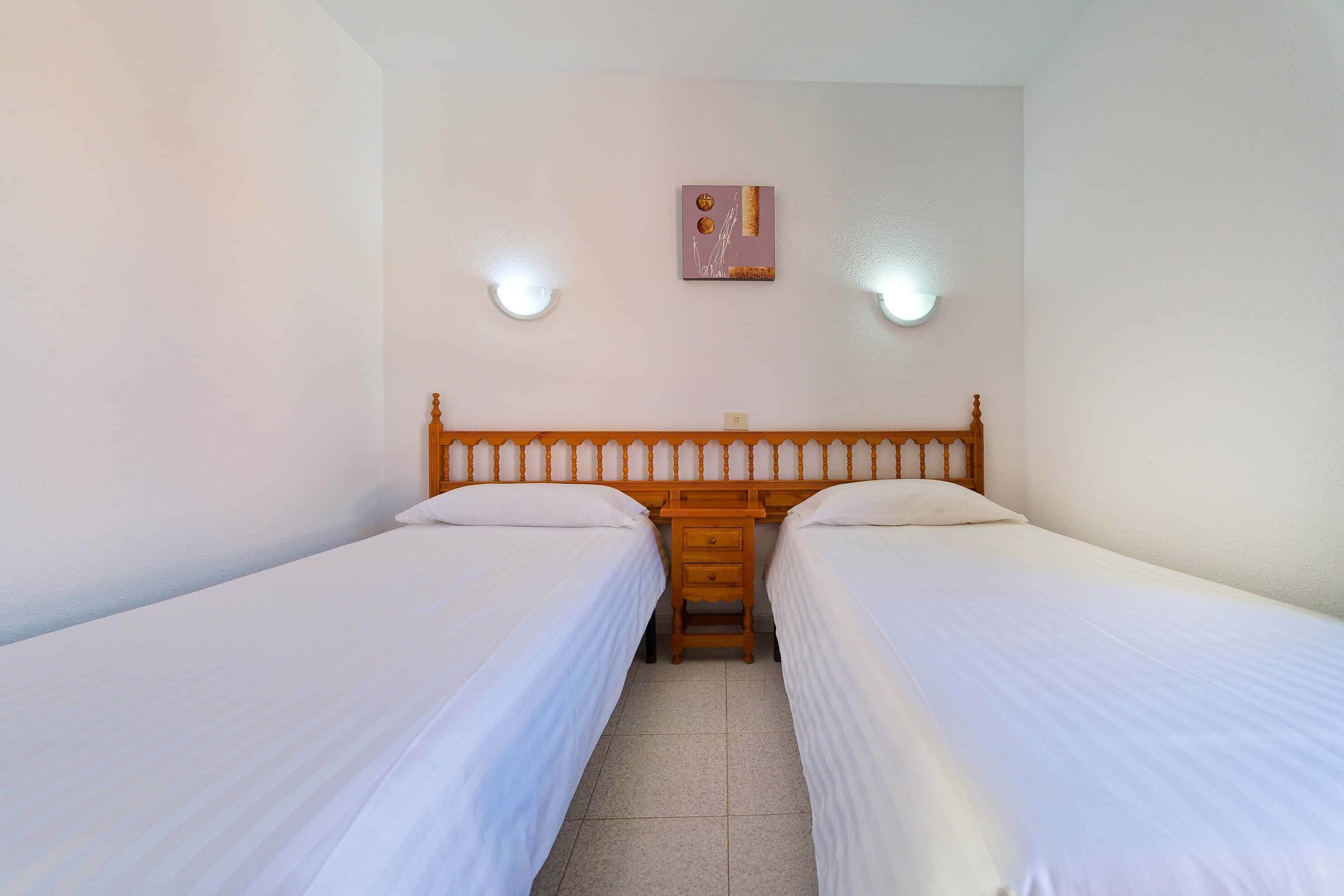 A twin room with two single beds, a wooden headboard, bedside tables, and wall-mounted lights.