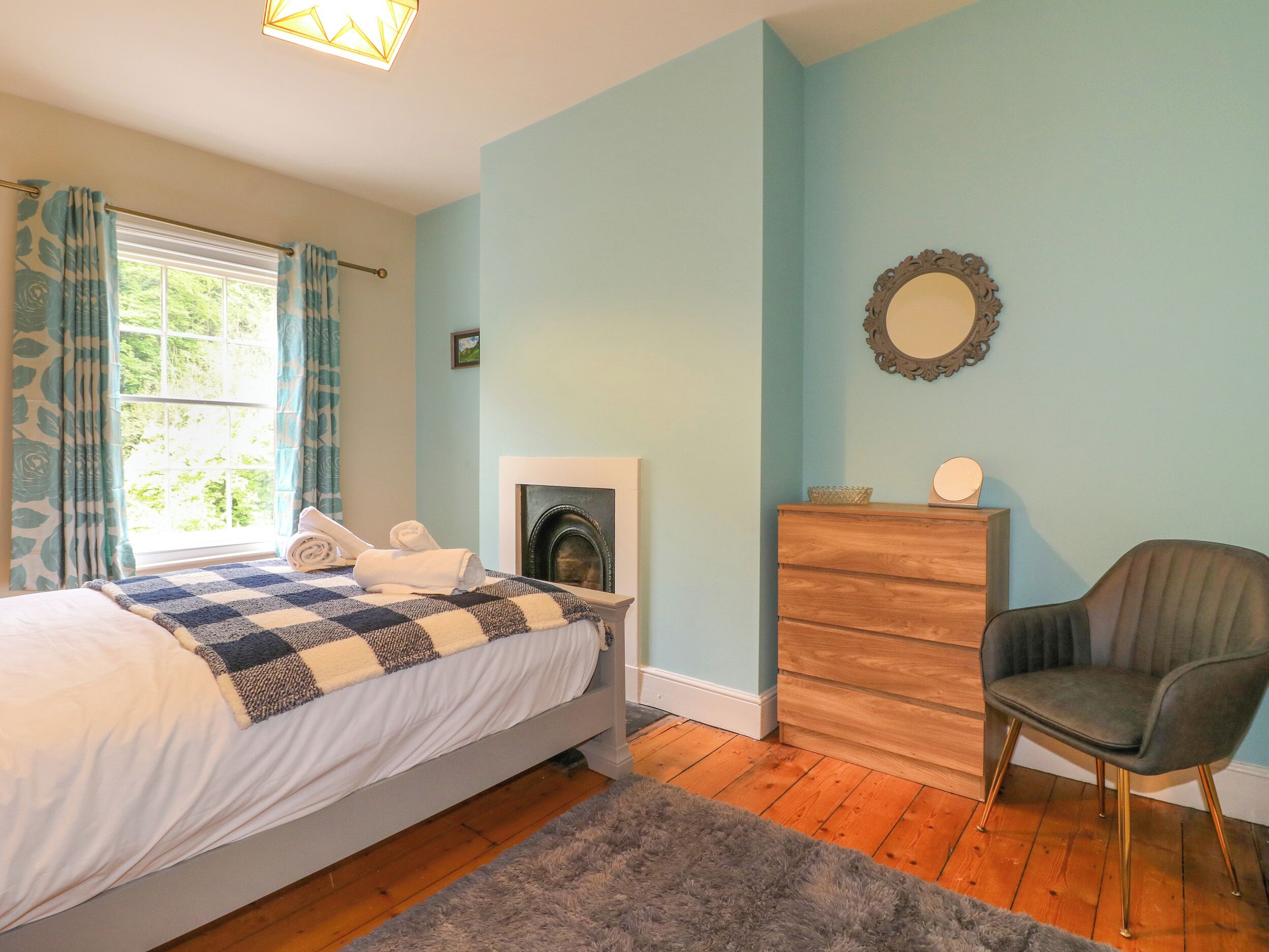 A bedroom with a bed, a dresser, a chair, a fireplace, and a window with curtains.