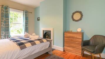 A bedroom with a bed, a dresser, a chair, a fireplace, and a window with curtains.