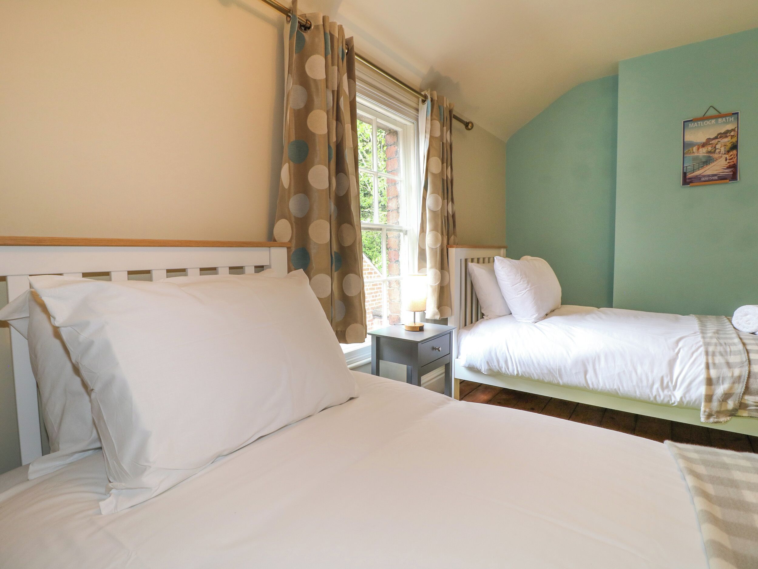 A bedroom with two single beds, a nightstand with a lamp, and a window with curtains.