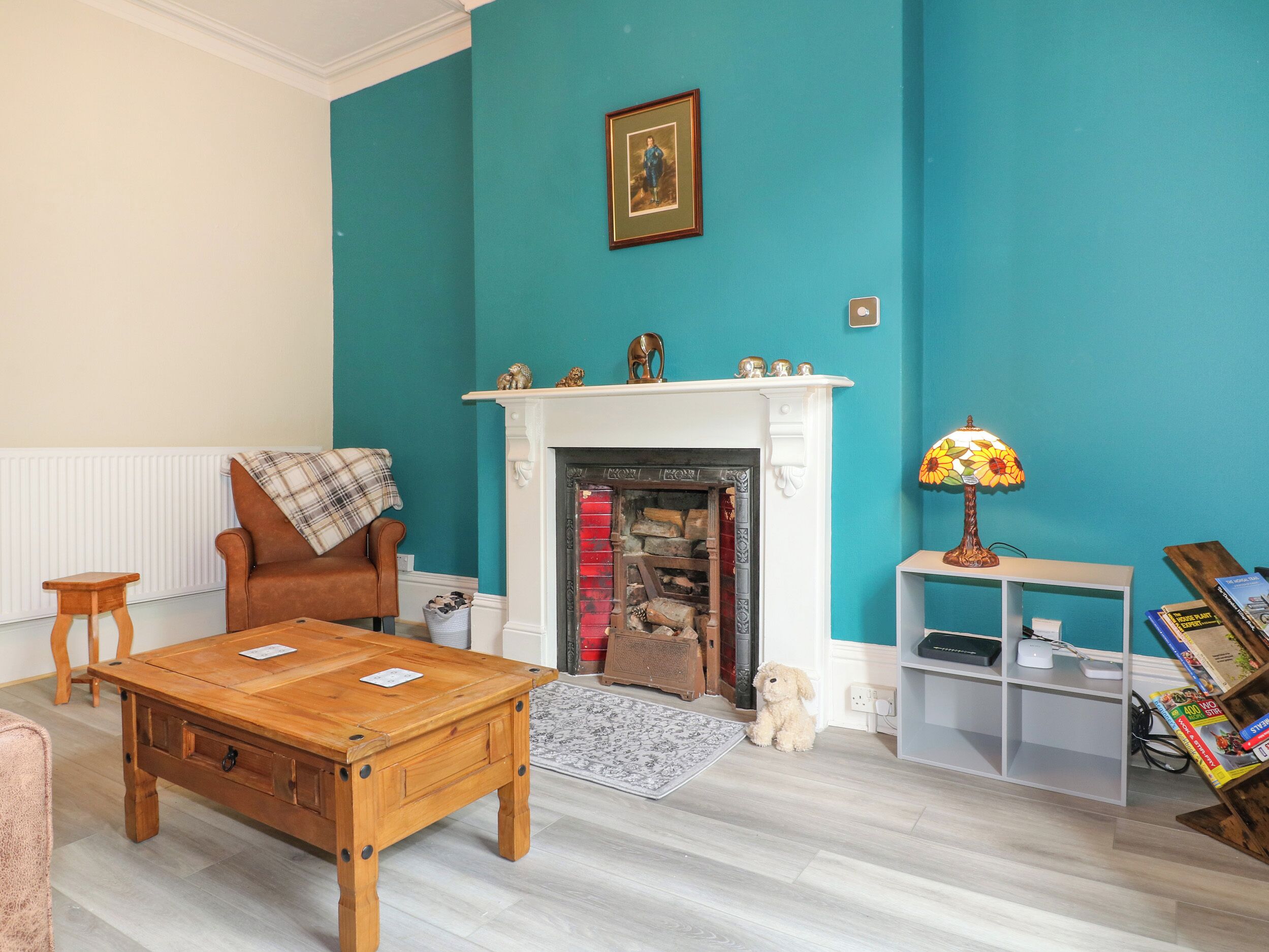A living room with teal walls, a fireplace, a brown leather chair, a wooden coffee table, and a small dog.