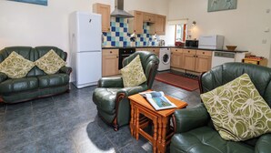 A compact living space with a kitchen, two green leather sofas with patterned cushions, a wooden coffee table, and a tiled backsplash. - Yr Hen Ysgubor (Carmarthen)