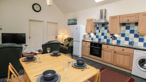 A compact kitchen with a dining area, a refrigerator, a washing machine, and a television. - Yr Hen Ysgubor (Carmarthen)