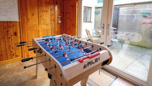 A foosball table in a room with wooden walls and a glass door leading to an outdoor area with chairs and a table. - Yr Hen Ysgubor (Carmarthen)