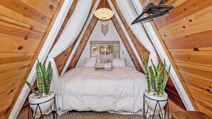 A cozy, triangular wooden room with a bed, two potted plants, and a hanging light fixture. - Acute A-frame Cabin w WiFi (Sugarloaf)