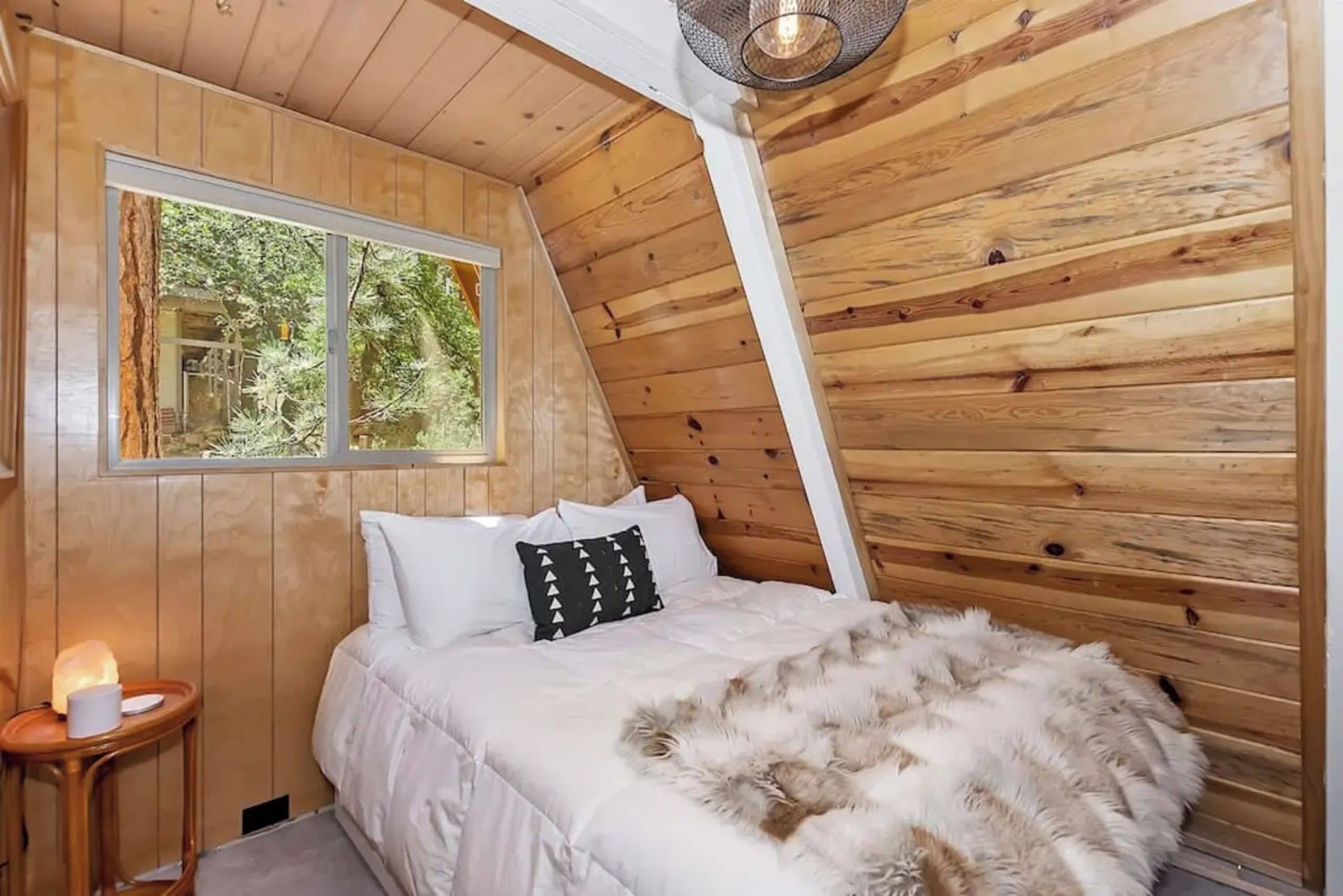 Ein gemütliches Schlafzimmer mit Holzwänden, einem Bett mit weißer Bettwäsche, einem flauschigen Teppich und einem kleinen Nachttisch mit Lampe.