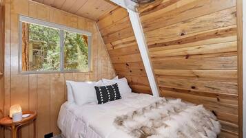 Ein gemütliches Schlafzimmer mit Holzwänden, einem Bett mit weißer Bettwäsche, einem flauschigen Teppich und einem kleinen Nachttisch mit Lampe.