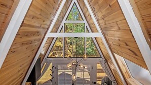 A triangular wooden ceiling with a skylight, a central chandelier, and a view of the outdoors. - Acute A-frame Cabin w WiFi (Sugarloaf)