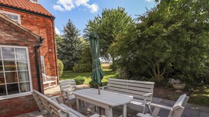 An outdoor patio with a white wooden table and chairs, a green umbrella, and a brick building in the background. - Moon Field Lodge (Scunthorpe)