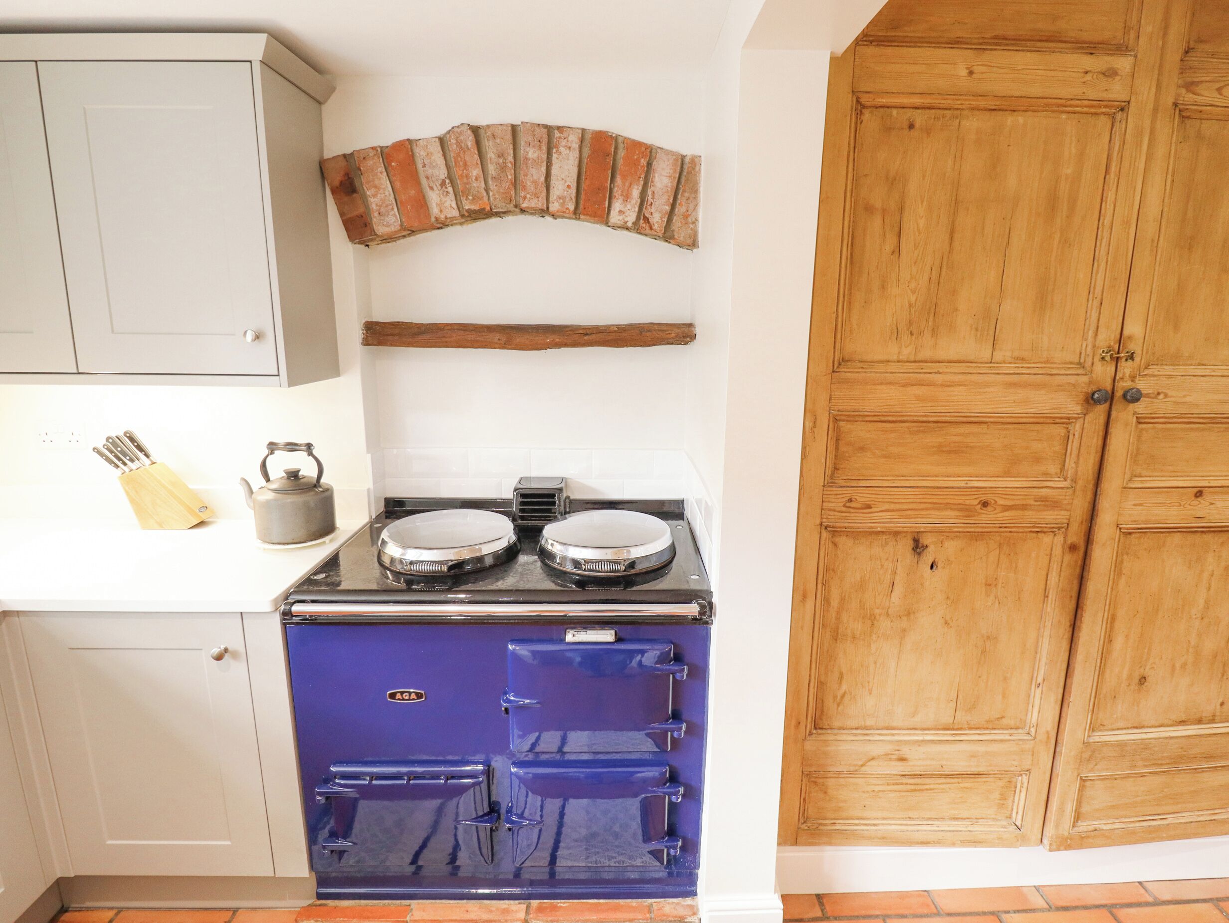 A kitchen with a blue stove, a brick arch, and wooden cabinets.