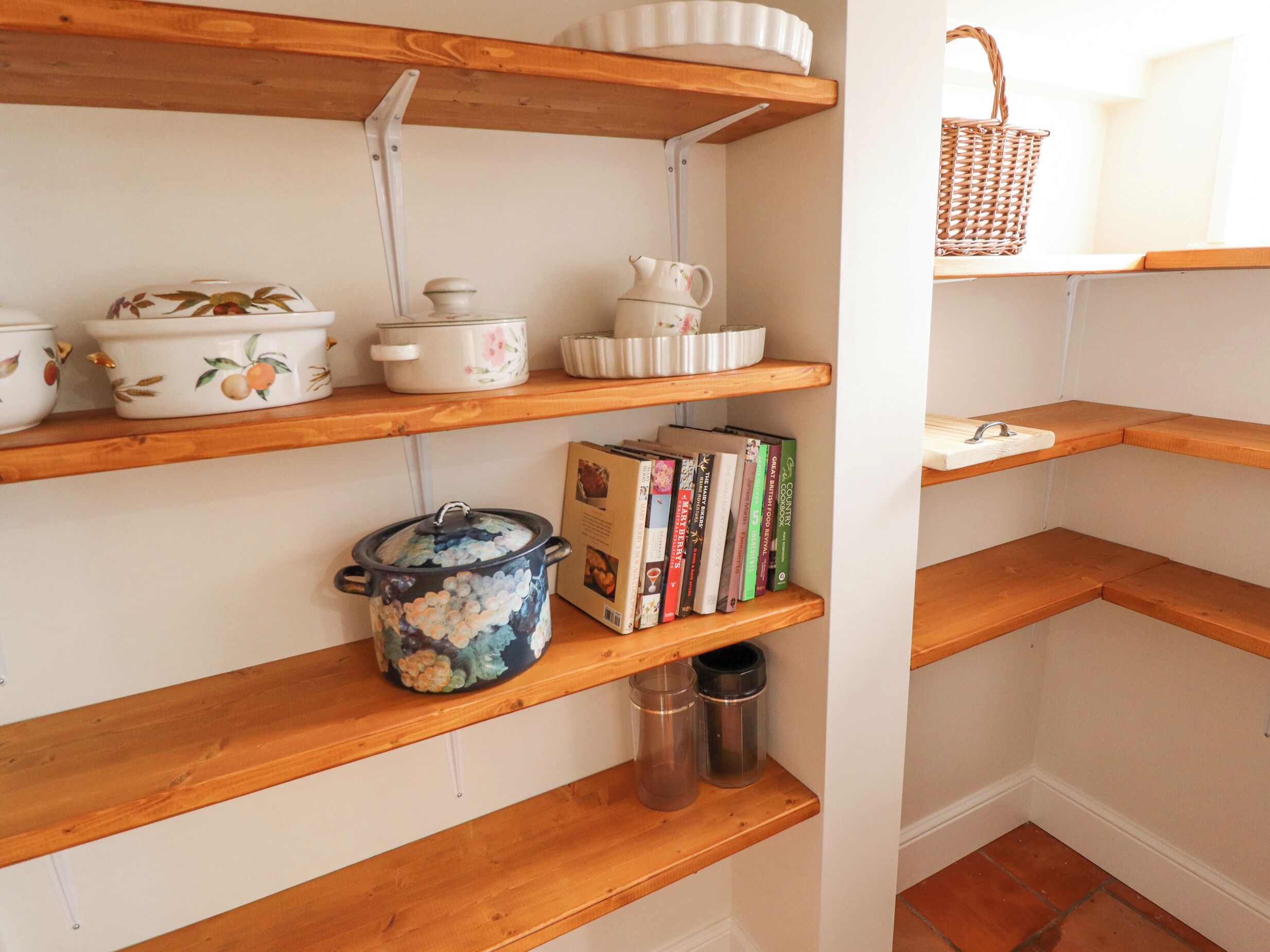 Una cocina con repisas de madera que sostienen utensilios de cocina, libros y una cesta.