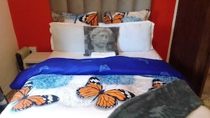 A bed with a blue and white bedspread featuring butterfly designs, white pillows, and a grey pillow with a black and white image. - Neo & ruks guest house goodwood (Cape Town)