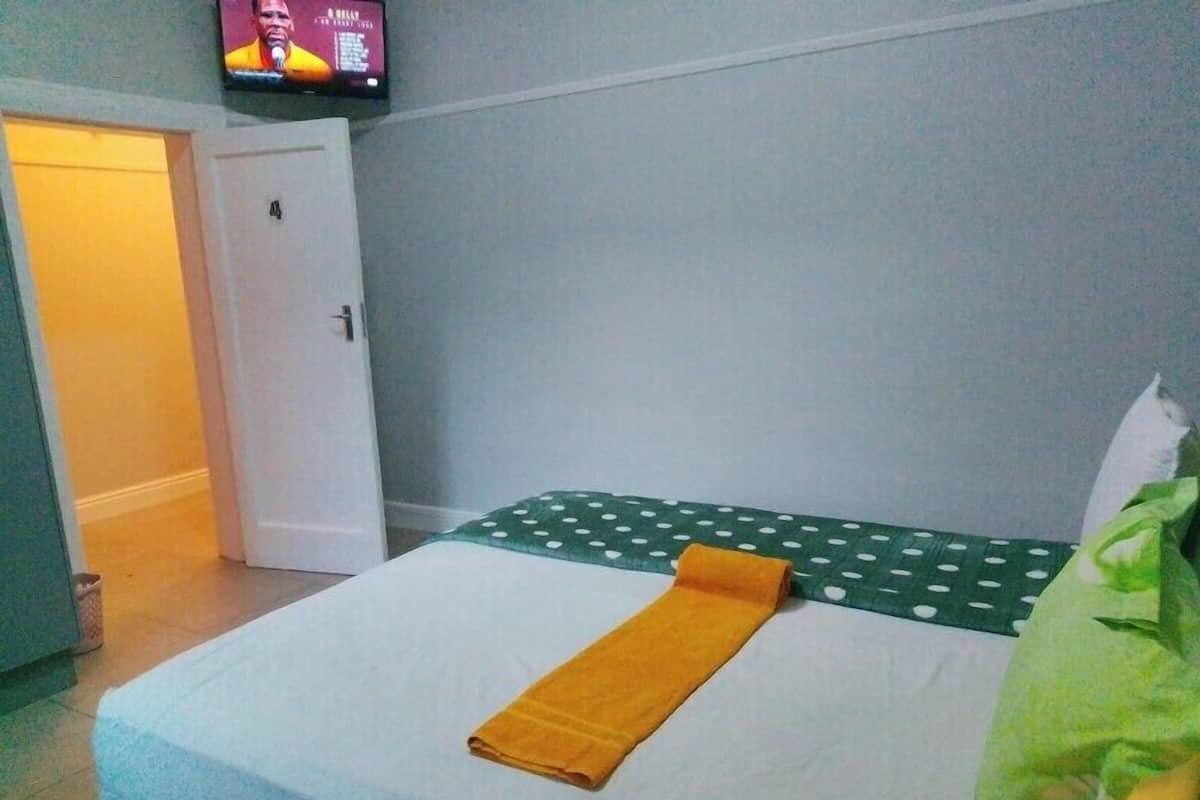 A hotel room with a bed, a television on the wall, and a door leading to another room.