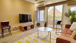 A living room with a flat-screen TV, a sofa, a coffee table, and a potted plant. - Xuru Stays I Spellbinding 2 BDR Apt. At The Giza Pyramid's Doorstep (Giza)