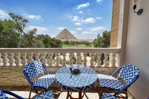 A balcony with a view of a pyramid, blue patterned chairs, and a small table with a decorative item. - Xuru Stays I Spellbinding 2 BDR Apt. At The Giza Pyramid's Doorstep (Giza)