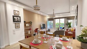 A dining area with a wooden table set for four, surrounded by chairs. There are framed pictures on the wall, a television, and a plant in the corner. - Xuru Stays I Spellbinding 2 BDR Apt. At The Giza Pyramid's Doorstep (Giza)